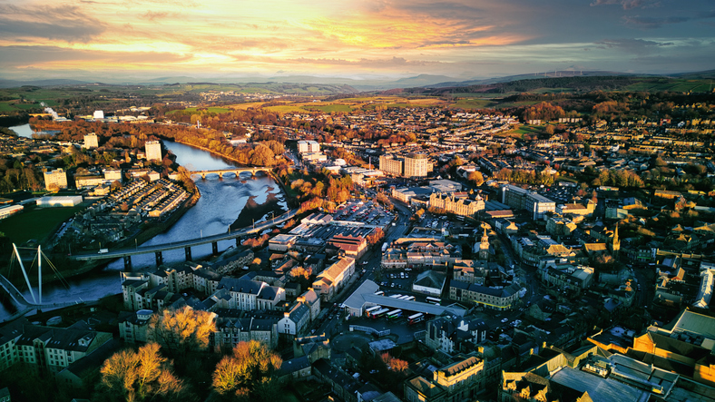 Aerial view of a city Lancaster at sunset with warm lighting, showcasing the urban landscape, buildings, and a river flowing through the center.